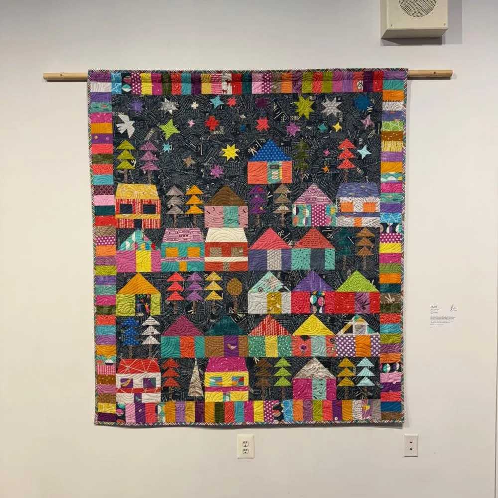 a piece of art created by weave. the patterns depict a village in a tapestry of lively colors.