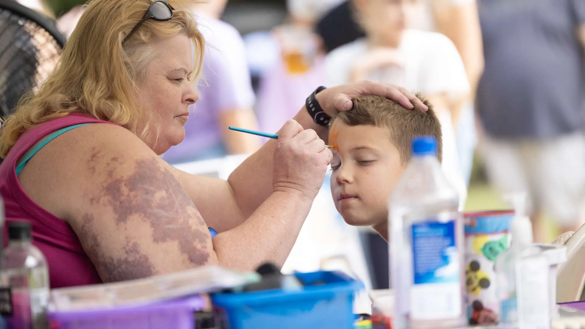 A woman is painting a younger man's face in one of the events of the festival.